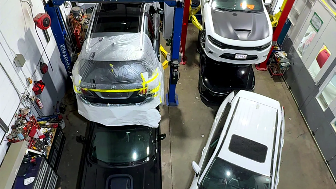 Elevated view across the Sultan Motors shop floor showing vehicles on hoists and a car masked for paint