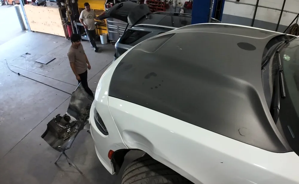 Sultan Motors repair bay with a Dodge Challenger on the floor, hood raised, and a technician crossing the shop