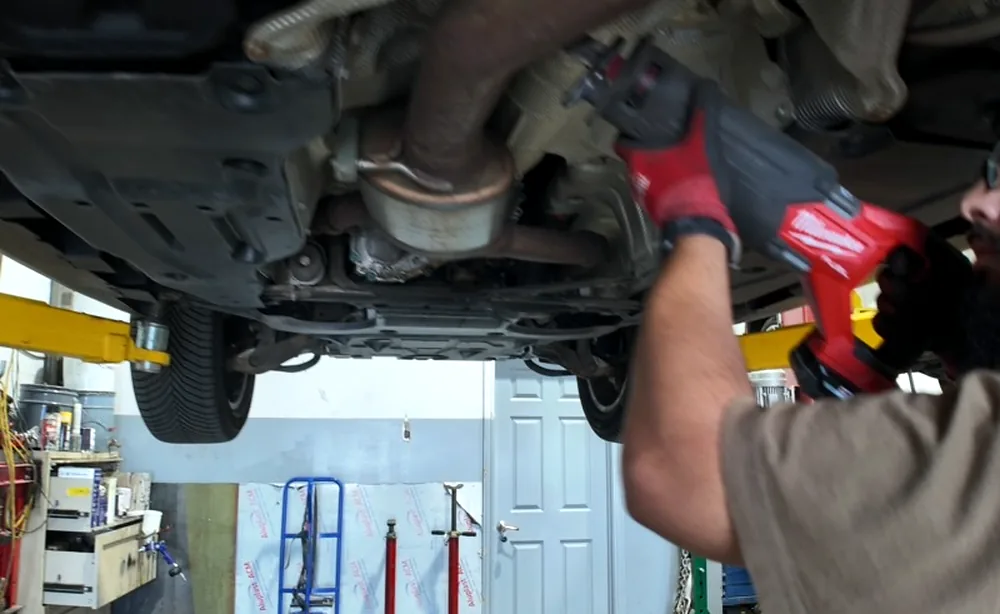 Technician using a cordless impact driver on exhaust hardware beneath a vehicle on the hoist at Sultan Motors