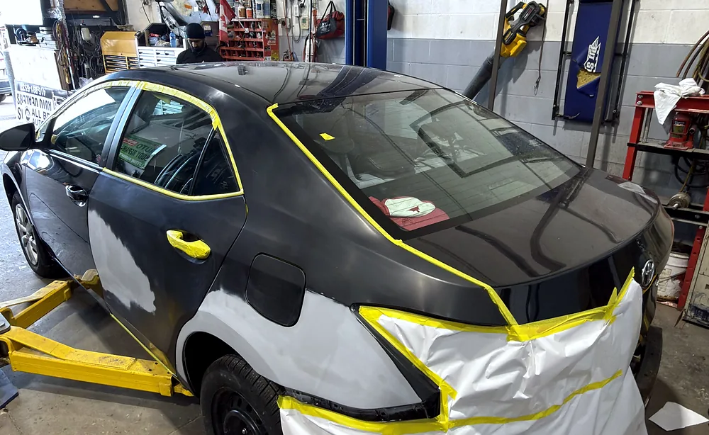 Sedan on the hoist with the fender and hood sanded to primer and masked with tape for refinishing