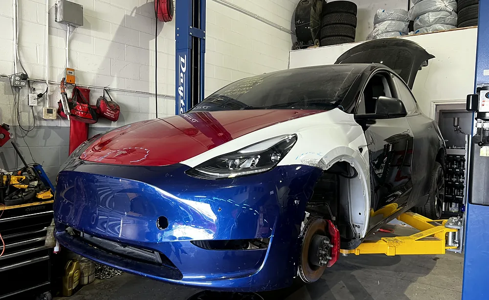 Tesla Model Y front end stripped on the hoist with the wheel off and brake assembly accessible