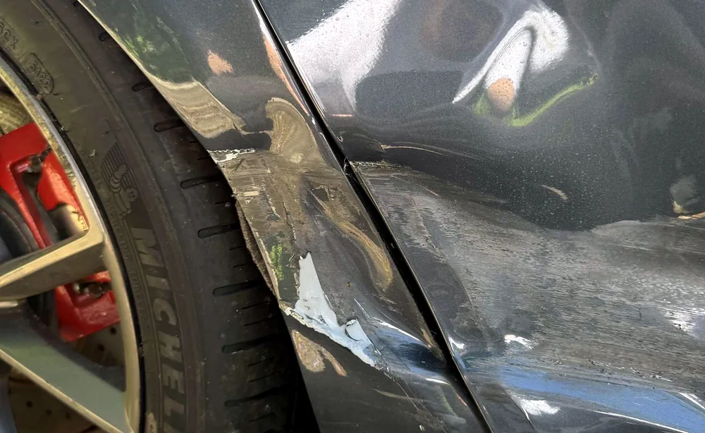 Technician's gloved hand tracing a panel crease above a wheel fitted with a red brake caliper