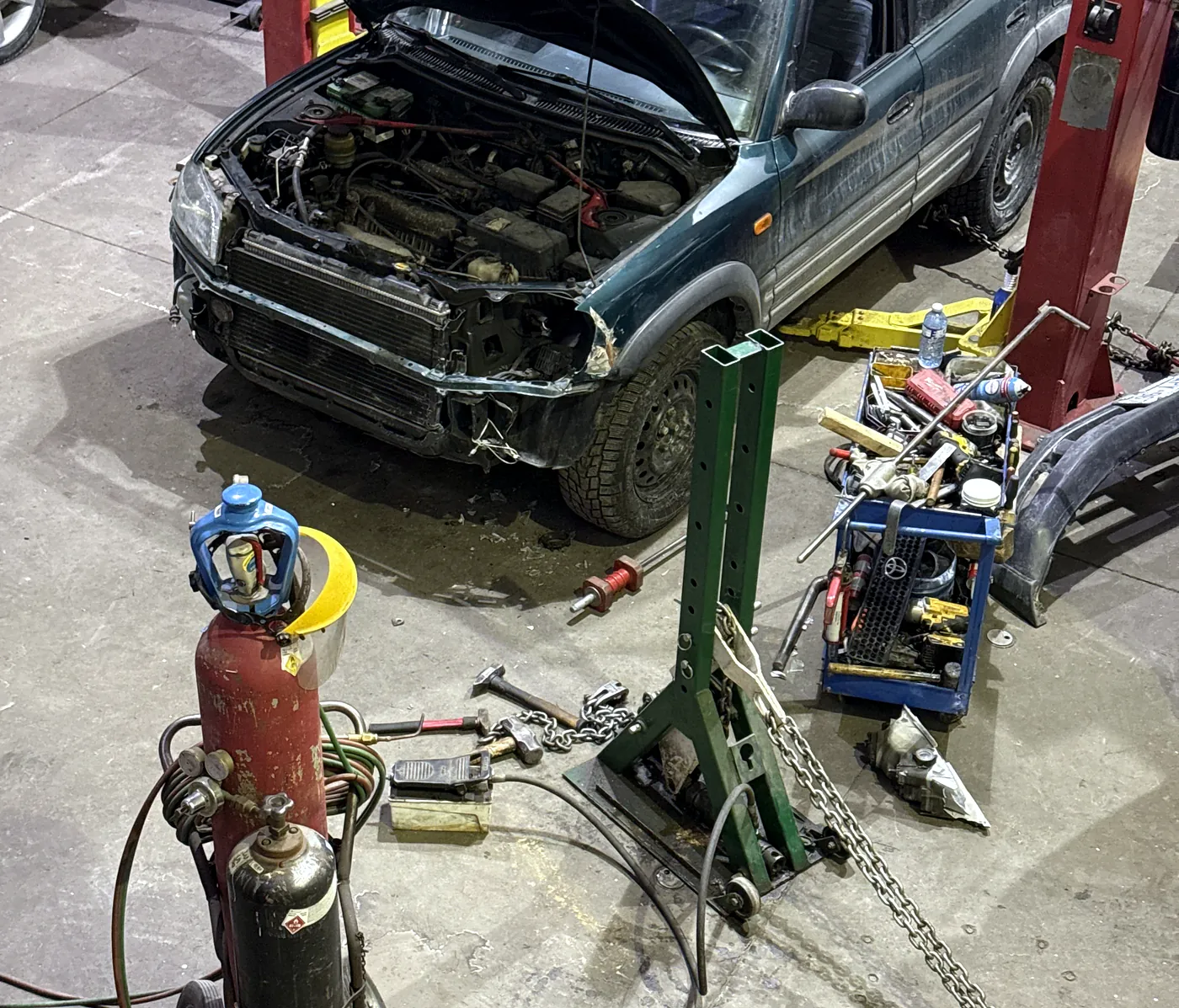 Collision-damaged Toyota RAV4 with the hood open and bumper removed beside pulling equipment at Sultan Motors
