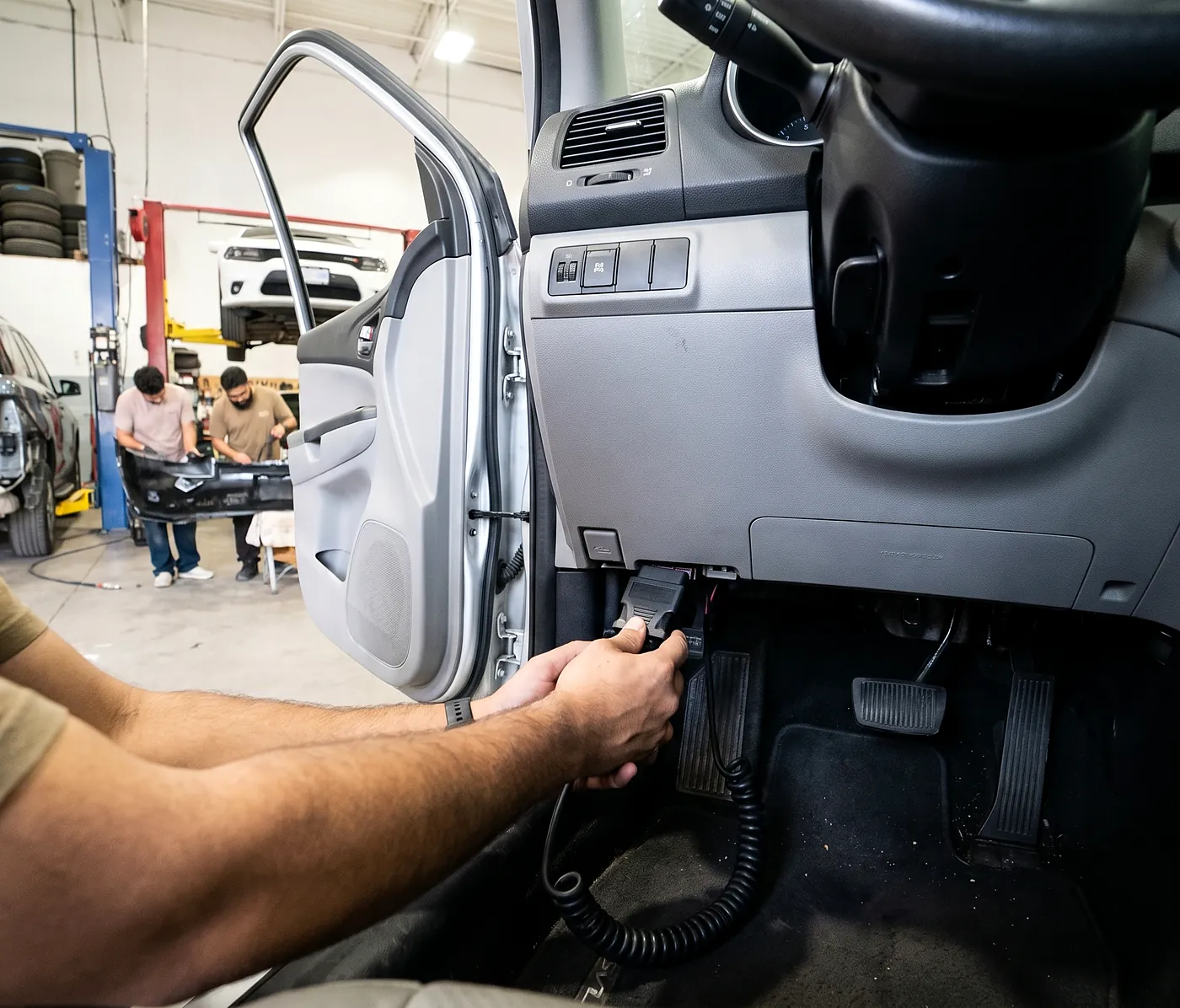 Technician connecting a diagnostic scan tool to the OBD-II port beneath a vehicle's dashboard