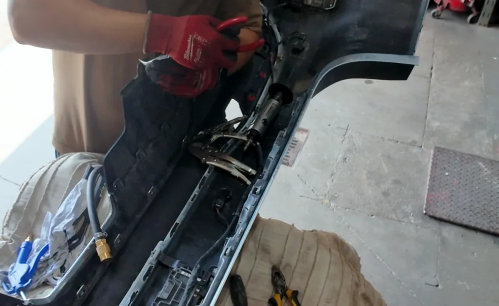 Technician in work gloves repairing exposed wiring inside a removed rear bumper assembly at Sultan Motors