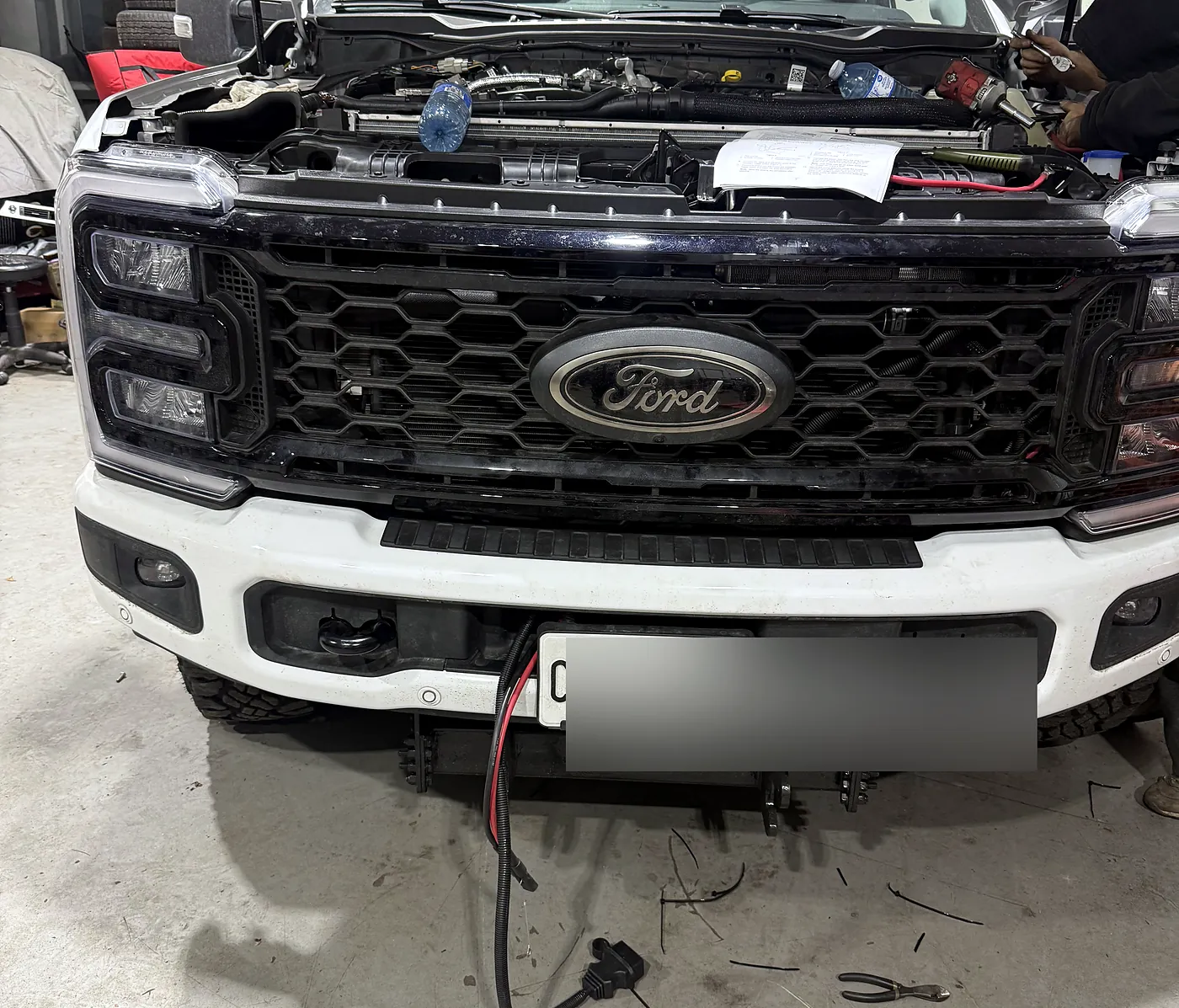 Ford pickup with the hood up and a wiring connector exposed below the bumper during electrical diagnosis