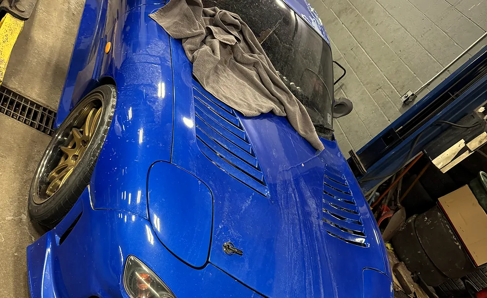 Sports coupe in a Sultan Motors bay with the hood raised for engine inspection