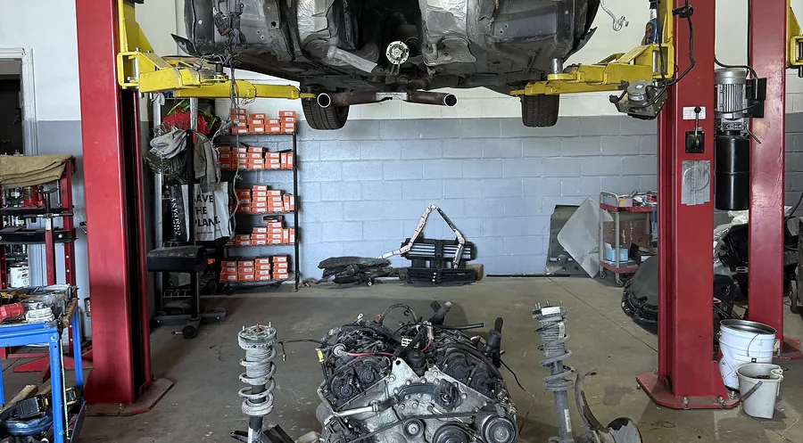 Engine and front subframe removed onto a shop dolly beneath a vehicle raised on a hoist at Sultan Motors