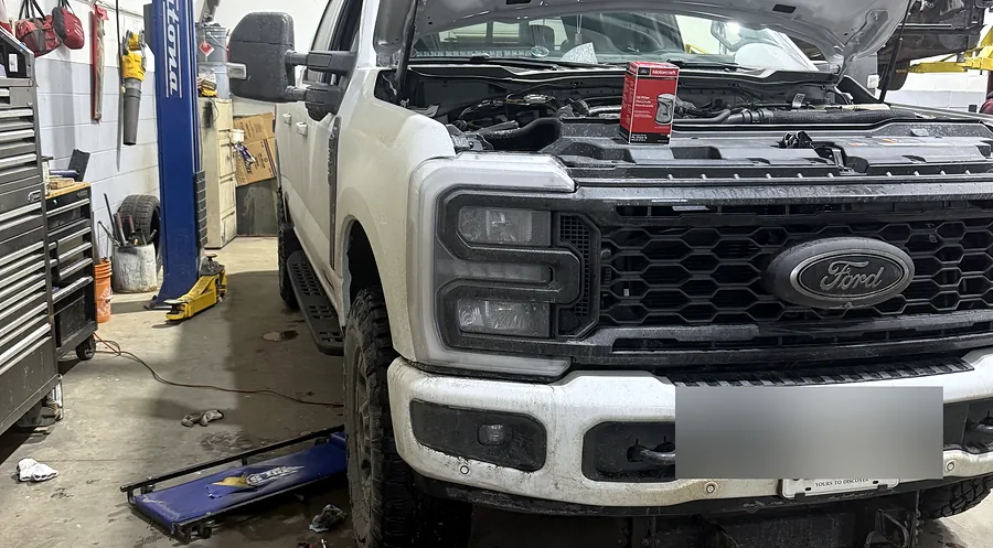 Fresh oil and a filter laid out beside a raised pickup truck before a scheduled oil service at Sultan Motors