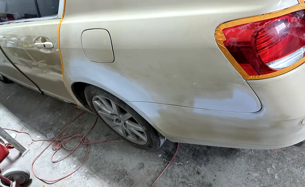 Rear quarter panel taped along the body lines with primer patches ready for a blended colour match