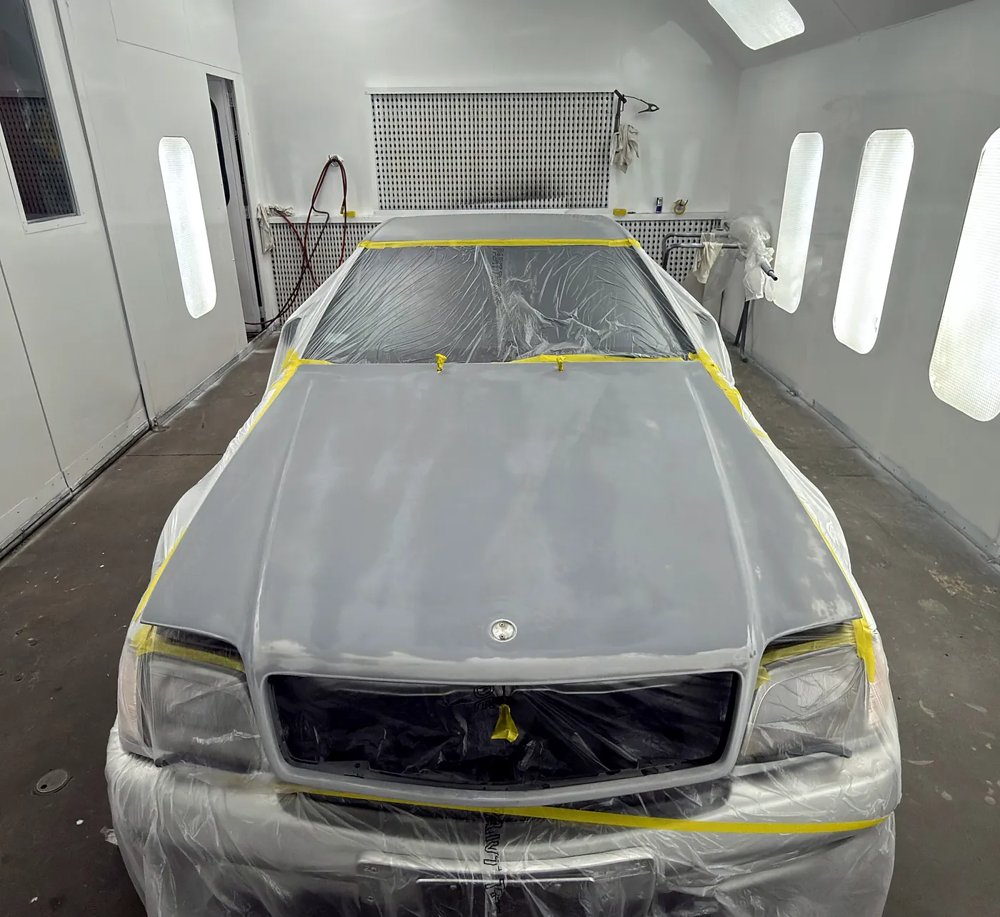 Coupe fully masked in plastic and tape, centred in the evenly lit Sultan Motors spray booth before painting