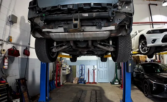 Vehicle underside on a two-post hoist showing subframe and suspension components
