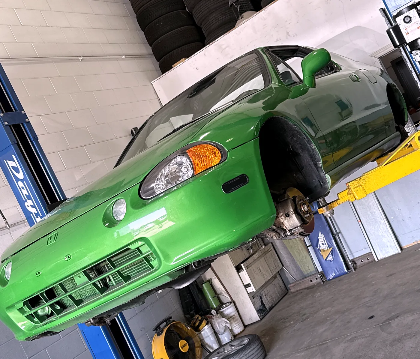 Honda Del Sol on a two-post hoist with the front corner stripped for suspension repair
