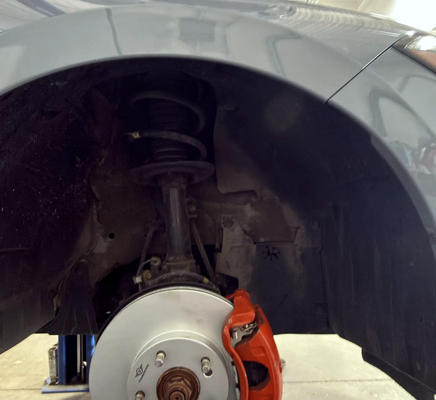 Front suspension strut and coil spring above a clean brake rotor and orange caliper inside the wheel arch